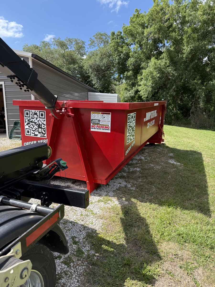 A red Dumpster Fire roll-off dumpster on a grassy Southwest Florida lot